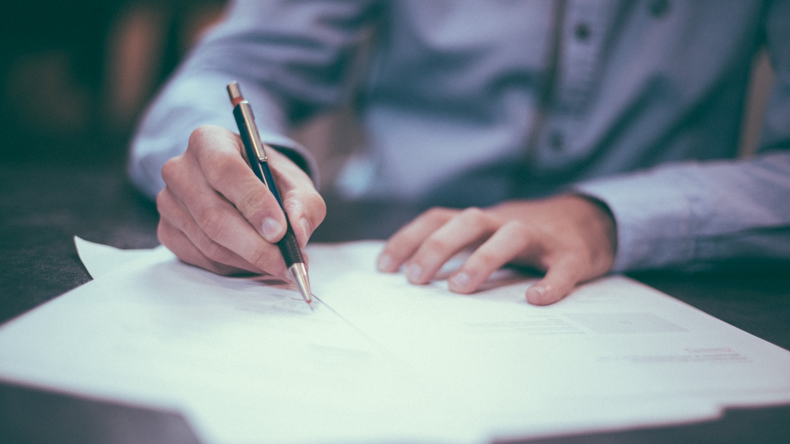 A hand signing a document with a pen — UAE property compliance, contracts, and tenancy registration.